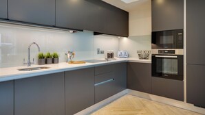 A modern kitchen with dark cabinets, a stainless steel sink, a microwave, and an oven. - The Benson Building (Dublin)