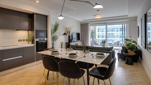 A modern kitchen with dark cabinets, a dining area with a table set for four, and a large window offering a view of the city. - The Benson Building (Dublin)