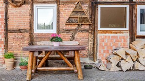 A rustic wooden table with a potted plant, a beehive, and stacked firewood against a brick wall with wooden beams. - Apartment Theo in the 'Alte Schule' Holiday Home with Mountain View, Shared Terrace & Wi-Fi (Ferna)