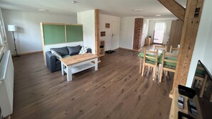 Amplia sala de estar con piso de madera, un sofá, una mesita y un comedor con sillas.