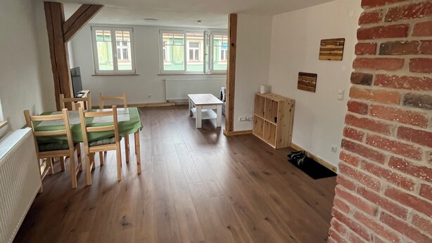 Una habitación espaciosa con piso de madera, un comedor con sillas y una mesa, y una chimenea de ladrillo.