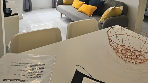 Una sala de estar moderna con un sofá, una mesa de comedor con un adorno y un ventanal con cortinas.