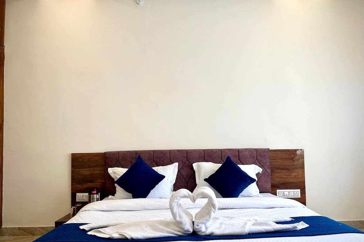 Cama bem arrumada com arranjo de toalhas em formato de coração, cabeceira de madeira e duas almofadas azuis.