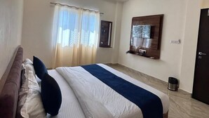 Ein Hotelzimmer mit einem großen Bett, einem Deckenventilator, einem an der Wand befestigten Fernseher und einer Tür.