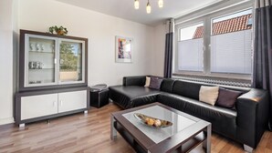 Una sala de estar moderna con un sofá, una mesa de centro de vidrio, un aparador con puertas de cristal y una ventana con cortinas.