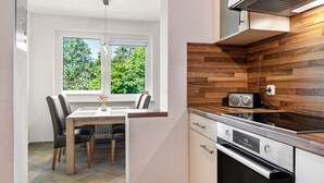 Una cocina moderna con horno empotrado, protector de fregadero de madera y ventana con vistas a zonas verdes.