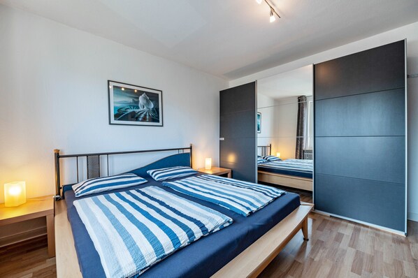 Une chambre à coucher moderne, avec un lit, des tables de chevet, une œuvre d’art accrochée au mur et un grand miroir.