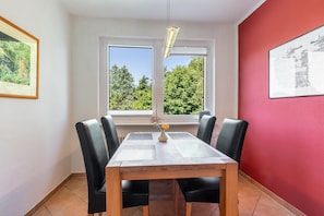 Un coin repas comprenant une table, des chaises, un vase avec des fleurs et une fenêtre donnant sur des arbres.