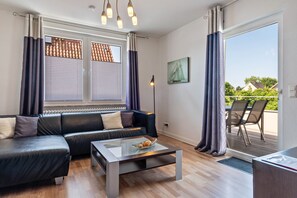Un salon moderne avec un canapé en cuir, une table basse en verre et une vue sur l’extérieur grâce à une porte-fenêtre coulissante.