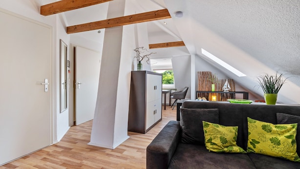 Ein modernes Interieur mit Holzboden, einem Sofa mit grünen floralen Kissen und einem Essbereich mit Tisch und Stühlen.