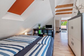A bedroom with a sloped ceiling, a bed with striped bedding, a bedside table with a lamp, a TV on a stand, and a wardrobe.