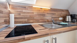 Eine moderne Küche mit Holzrückwand, integriertem Induktionskochfeld, Spüle aus Edelstahl und Geschirrgestell.
