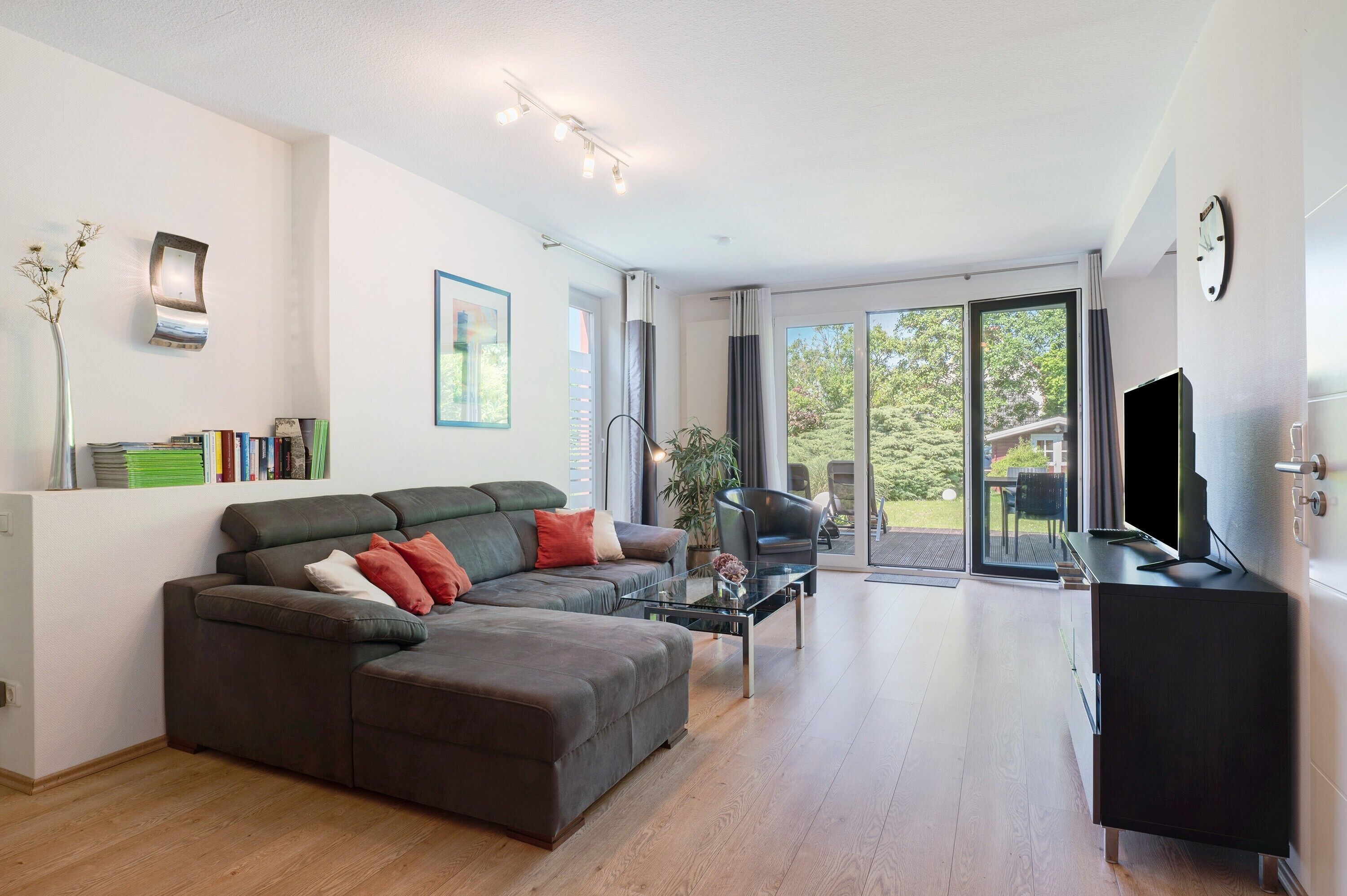 Een moderne woonkamer met een hoekbank, salontafel, televisie en een schuifdeur naar een buitenruimte.