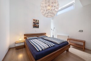 A bedroom with a bed, bedside tables, a bench, a hanging light fixture, and a framed picture on the wall.