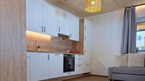 A modern kitchen with white cabinets, a wooden ceiling, and a hanging light fixture. - Mountain Lodge (Flachau)