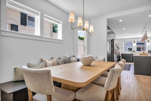 A modern kitchen with a central island, a dining area with a wooden table and upholstered chairs, and a pendant light fixture.