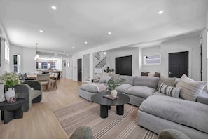 A modern living room with a grey sectional sofa, a round coffee table, and a dining area in the background.