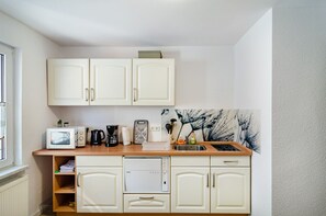 A compact kitchen with white cabinets, a microwave, a coffee maker, and a Bosch dishwasher.