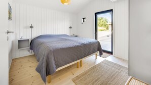 Une chambre moderne avec un lit, des tables de chevet, une lampe sur pied et une vue sur l’extérieur grâce à une porte coulissante.