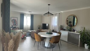 Uma sala de estar moderna com uma mesa de jantar redonda, dois sofás, uma TV e um espelho grande.