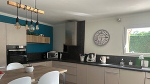 Cozinha moderna com área de refeições, apresentando uma mesa de madeira, cadeiras brancas, bancada preta e um relógio na parede.