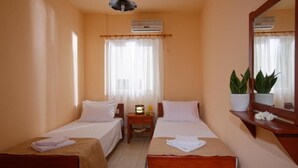 A hotel room with two single beds, a small bedside table with a lamp, a potted plant, and a mirror on the wall. - Semeli Stalis (Stalida)