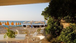 An outdoor seating area with tables and chairs, overlooking a beach with umbrellas and lounge chairs. - Semeli Stalis (Stalida)