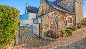 Un bâtiment en pierre avec une allée pavée, une clôture blanche et un petit jardin agrémenté d’arbustes.