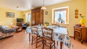 A dining area with a table set for four, wooden chairs, a television, and a window with curtains. - Holiday Home 'Maison De Caractère' with Wi-Fi (Roscoff)