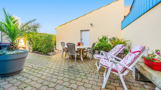Une terrasse avec une table et des chaises, un pot de fleurs et un petit bâtiment doté d’une porte.