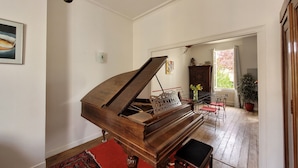 A grand piano in a spacious room with a red carpet, a wooden floor, and a view of a garden through an open door.
