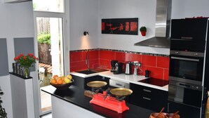 A modern kitchen with red and black appliances, a large island with a red scale, and a view of the backyard.