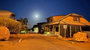 Eine Wohnstraße bei Nacht mit Häusern an beiden Seiten, einem klaren Himmel und einem sichtbaren Mond.