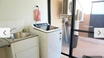Une cuisine équipée d’un lave-linge, d’un évier et d’une fenêtre donnant sur un patio.