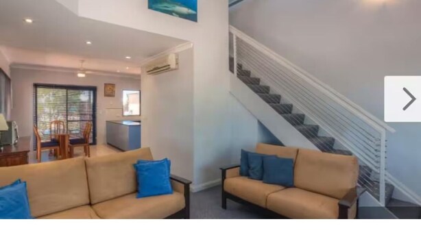 Ein modernes Wohnzimmer mit einem beigen Sofa, einem Essbereich mit Tisch und Stühlen sowie einer Treppe mit Geländer.
