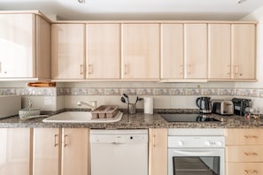 Een keuken met lichte houten kastjes, een granieten aanrechtblad, een Bosch vaatwasser en een Thermador oven.