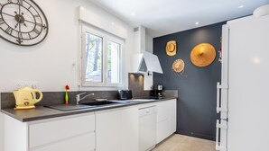 A modern kitchen with a large window, a clock, and decorative wall art. - Family House 400m from the Beach - La Grière Plage (La Tranche sur mer)