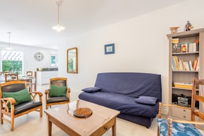 A living room with a sofa, chairs, a coffee table, a bookshelf, and a dining area with chairs and a table. - Family House 400m from the Beach - La Grière Plage (La Tranche sur mer)