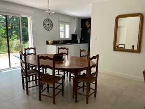 A dining area with a wooden table and chairs, a kitchen in the background, and a large mirror on the wall.