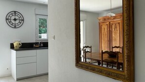 A modern kitchen with white cabinets, a black countertop, a clock, and a large mirror on the wall. - Family House 400m from the Beach - La Grière Plage (La Tranche sur mer)