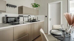 Une cuisine moderne  équipée d’un four à micro-ondes, d’une cuisinière et d’un évier intégrés. On y trouve un coin repas avec une table dressée pour deux personnes, ainsi qu’une porte donnant sur une autre pièce.