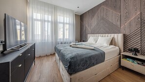 Une chambre moderne avec un grand lit, un téléviseur posé sur un meuble et un mur décoré d’un motif en bois.