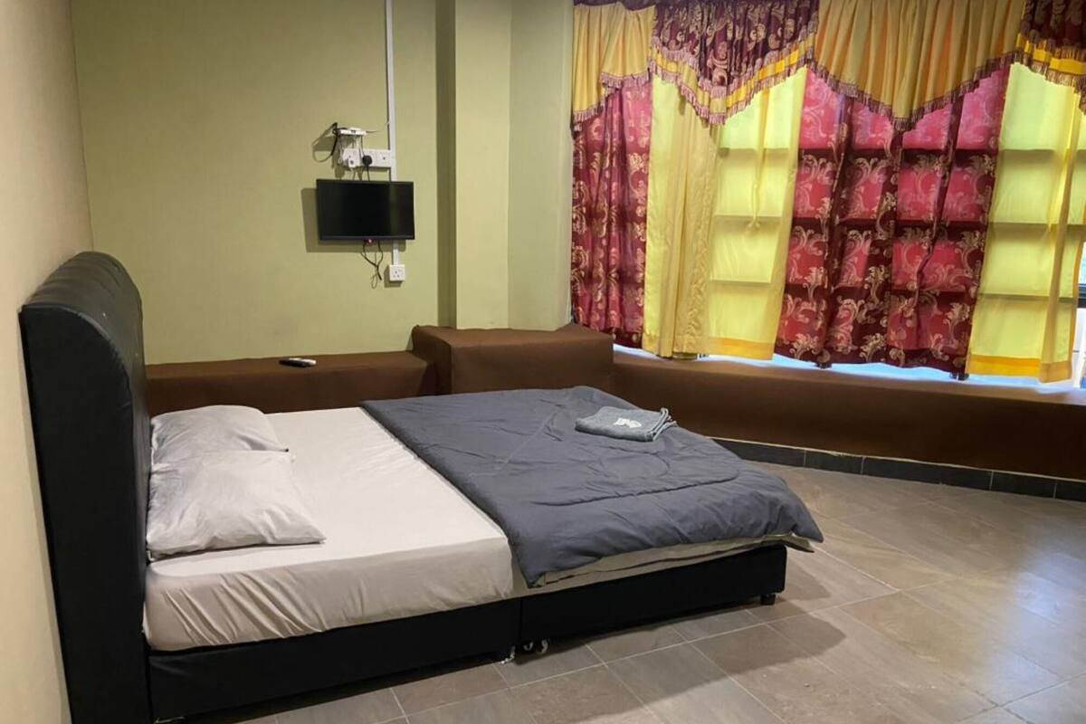 A bedroom with a bed, a TV mounted on the wall, and curtains.