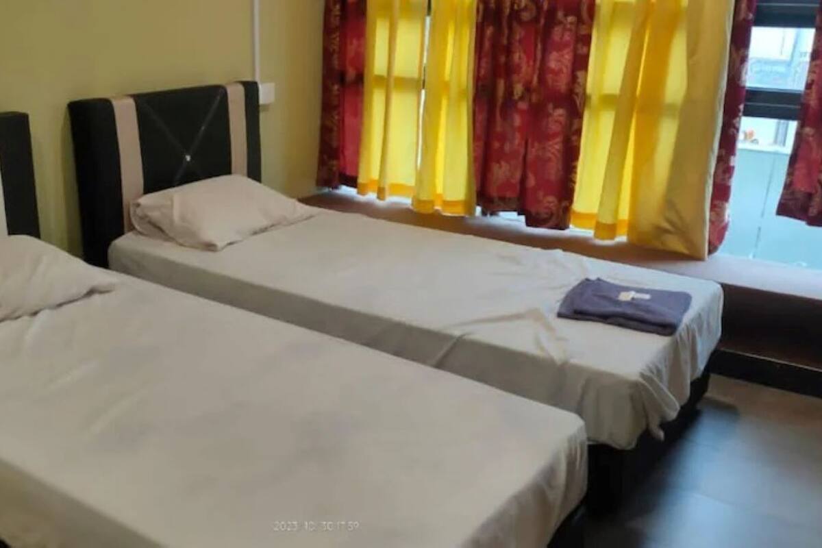 Two single beds with white linens in a room with yellow curtains and a window.