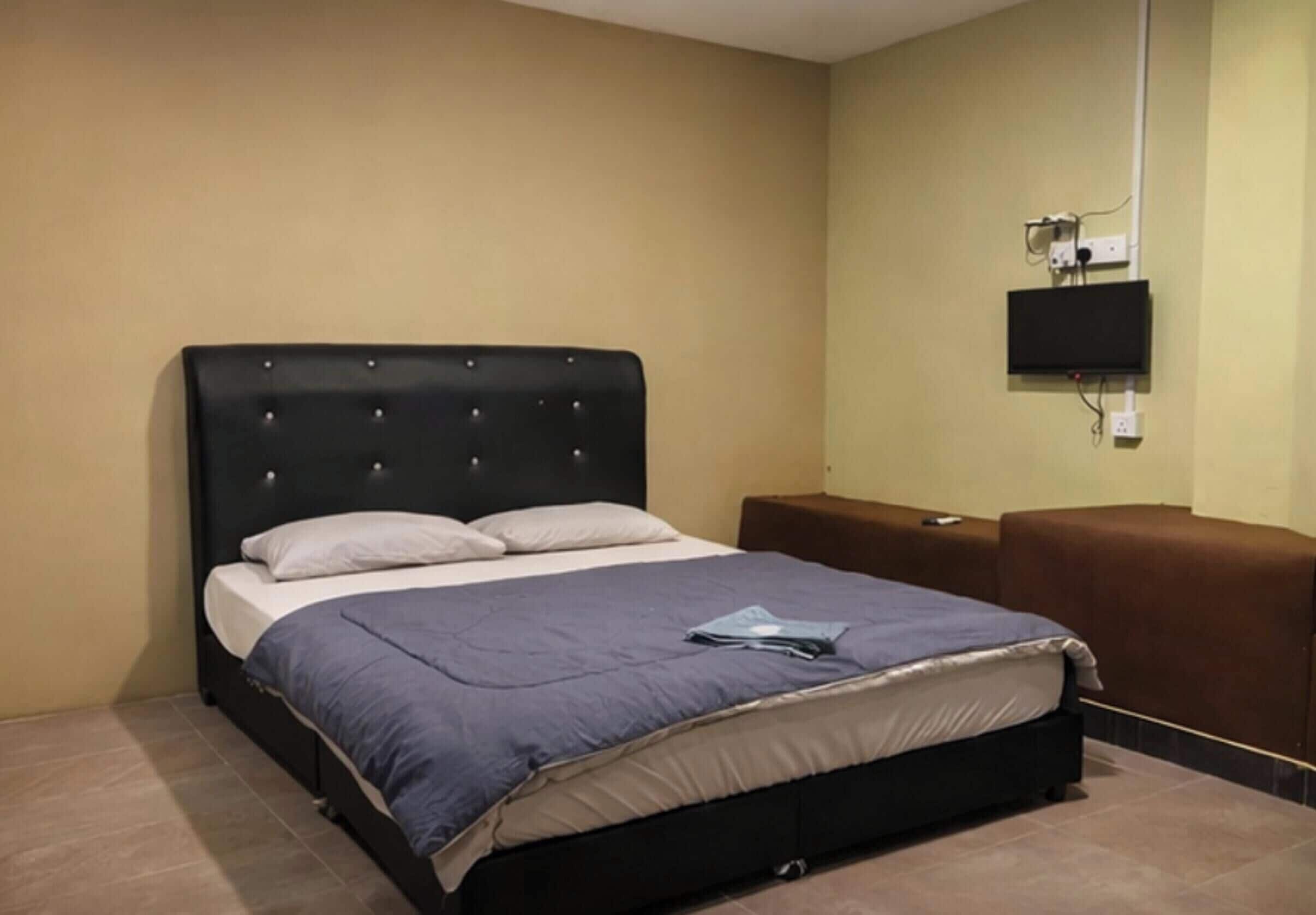 A hotel room with a bed, a flat-screen TV mounted on the wall, and a brown sofa.