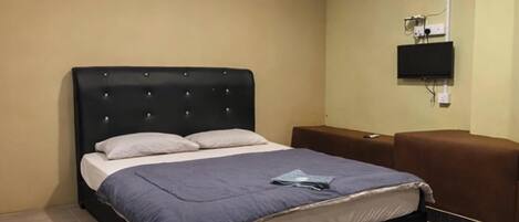 A hotel room with a bed, a flat-screen TV mounted on the wall, and a brown sofa.