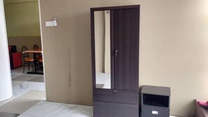 A room with a closed door, a dark-colored wardrobe, a small trash bin, and a tiled floor.