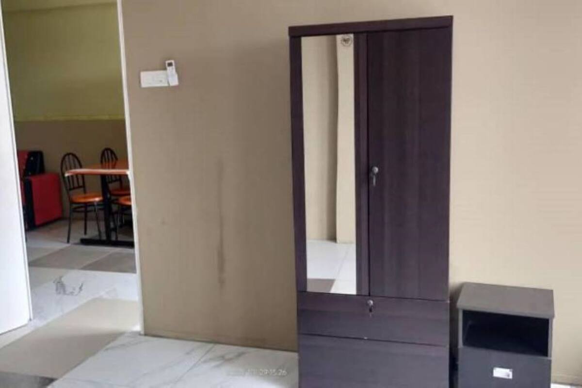 A room with a closed door, a dark-colored wardrobe, a small trash bin, and a tiled floor.