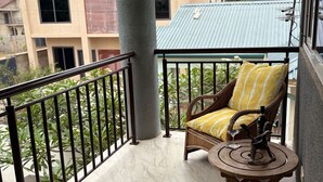 A balcony with a wicker chair, a small round table, and a view of buildings in the background.