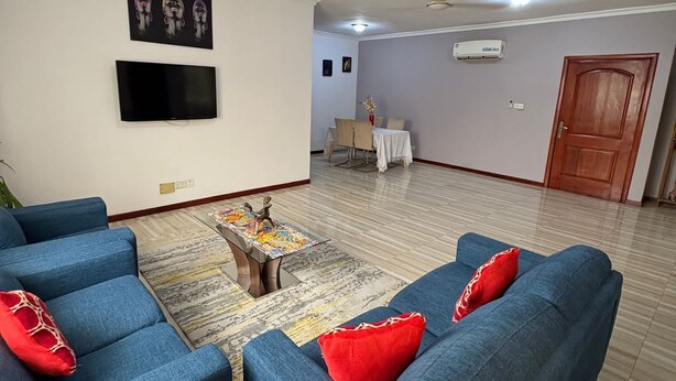 A living room with a blue sofa set, a flat-screen TV, and a dining area with a table and chairs.